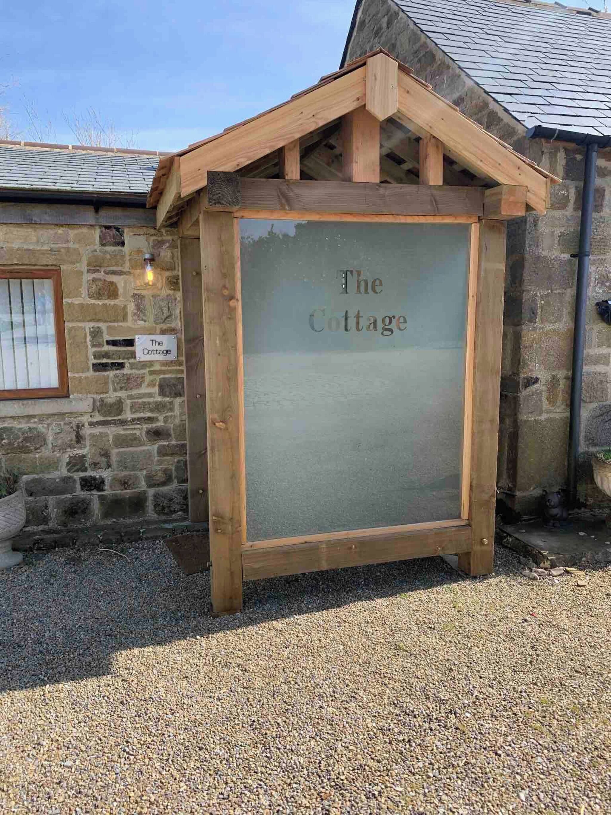 Une petite maison en bois avec une pancarte indiquant « The Cottage » devant une allée gravillonnée.