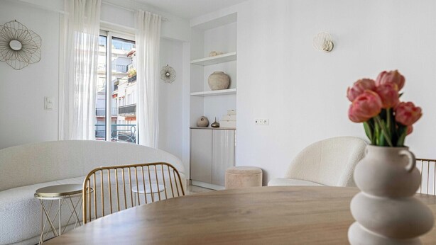 Ein stilvolles Wohnzimmer mit einer Couch, einem runden Holztisch und einer Vase mit Blumen.