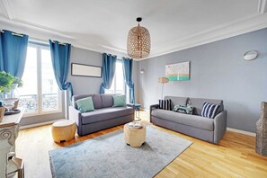 A living room with two sofas, a wooden ottoman, a hanging light fixture, and a view of the outdoors. - Comfortable Apartment 1BR/4P - Champs Élysées (Paris)