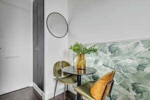 A room with a round table, two chairs, a potted plant, a wall-mounted mirror, and a door. - Charming Studio Apartment - AC- 2P - Nation (Paris)