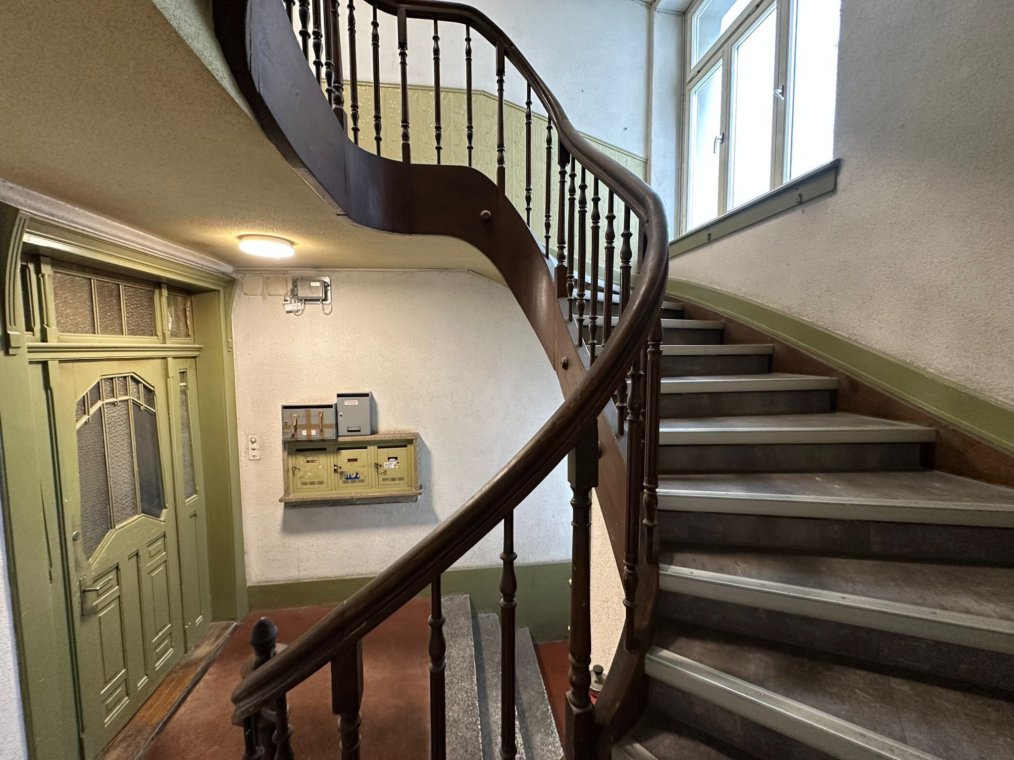 Un escalier avec une rampe en bois et une porte verte dotée d’une fenêtre.