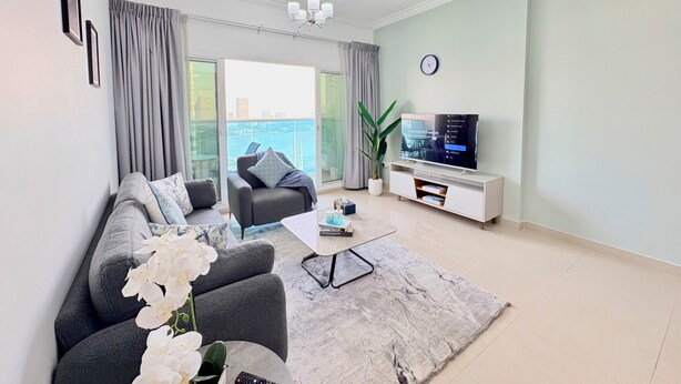 Ein modernes Wohnzimmer mit Sofa, Couchtisch, Fernseher und einem Balkon mit Blick auf die Stadt.