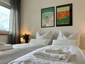 Una habitación de hotel con dos camas, una ventana con cortinas, un jarrón con flores y dos carteles de viajes enmarcados en la pared.