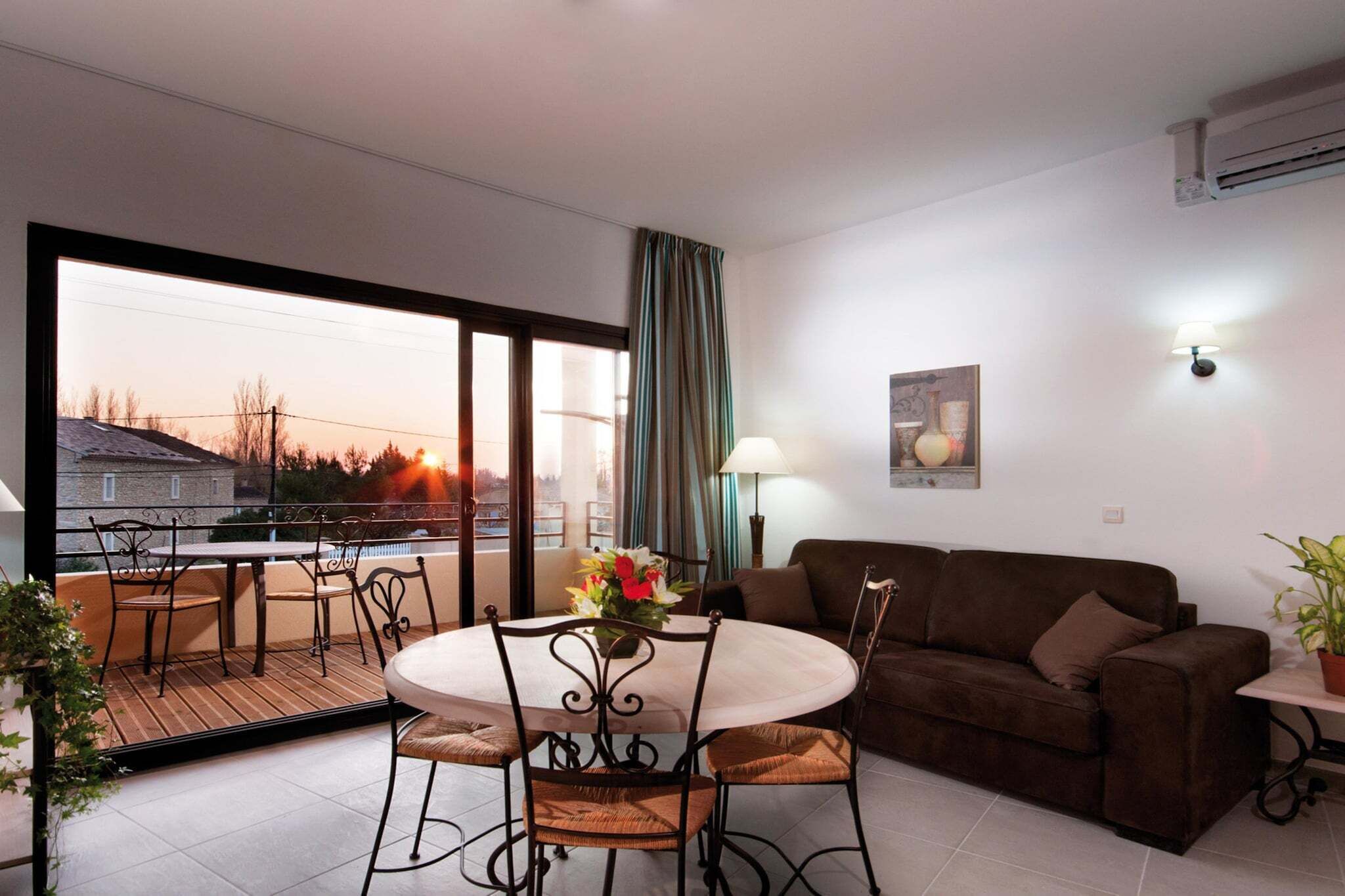 A room with a balcony, a round table with chairs, a sofa, and a lamp.
