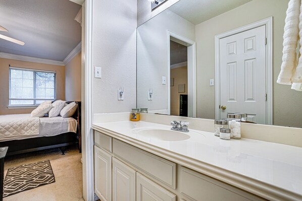 A bedroom with a bed, a large mirror, a bathroom with a sink and mirror, and a window with blinds.