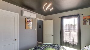 A bedroom with a bed, an air conditioning unit, a door, a window with curtains, and a wall with a poster. - Alien-Crash-Site-Themed Retreat in Roswell (Roswell)