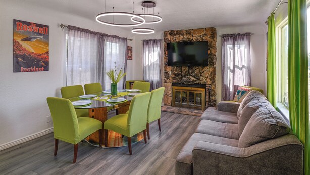 A living room with a fireplace, a dining area with green chairs, a sofa, and a TV mounted on the wall. - Alien-Crash-Site-Themed Retreat in Roswell (Roswell)