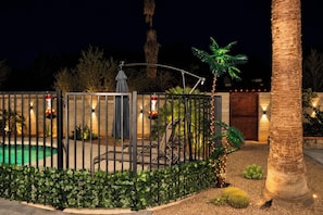 A well-lit outdoor area with a swimming pool, a metal fence, and various plants. - Pool, Hot Tub, Outdoor Kitchen, Near I10 (Tucson)