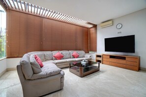 Una sala de estar con sofá, mesa de centro, televisor y persianas.