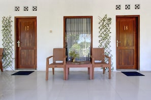 A room with two wooden doors, numbered 17 and 18, a window with a curtain, and two wicker chairs with a small table in between.