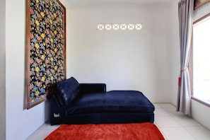 Une pièce avec un canapé bleu foncé, un tapis rouge, une œuvre d’art florale accrochée au mur et une fenêtre avec des rideaux.