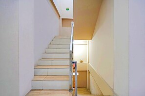 Een smalle trap met een metalen leuning, witte muren en een klein raam aan de bovenkant.