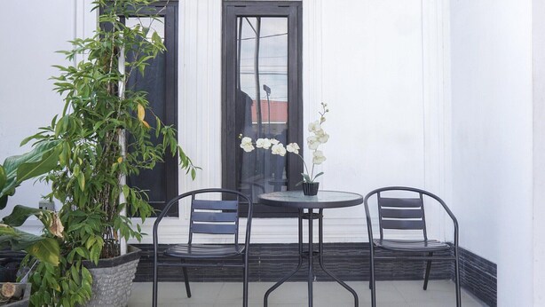 Un pequeño espacio al aire libre con una mesa, dos sillas, una planta en maceta y una puerta con reflejos.