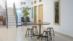 Un interior moderno con una escalera, una mesa redonda con taburetes, una planta en maceta y un ventanal.