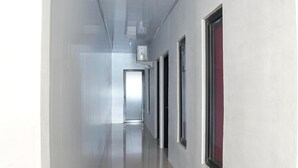 Un pasillo largo y estrecho con suelo reflectante, puertas a un lado y una lámpara en el techo.