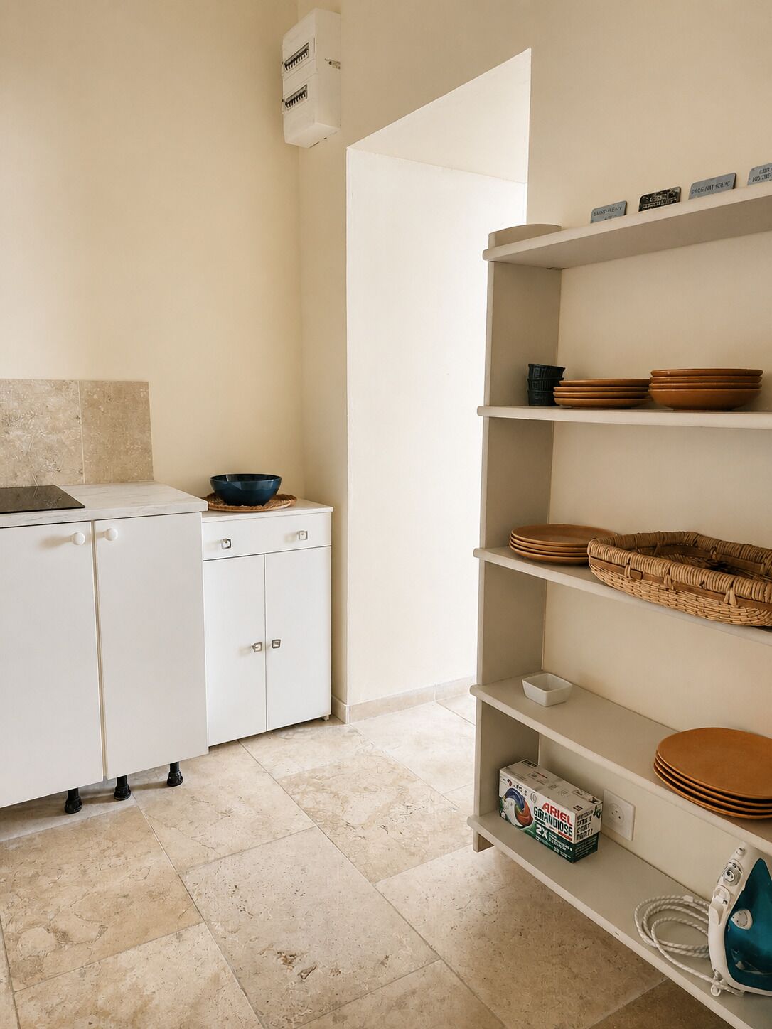 A kitchen with white cabinets, a sink, and a shelf with dishes and a basket.