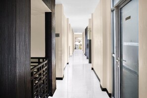 A corridor with a wooden railing, a door with a sign, and a tiled floor.