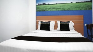 Una cama con ropa de cama blanca, cabecera marrón y un mural de un campo verde en la pared de fondo.