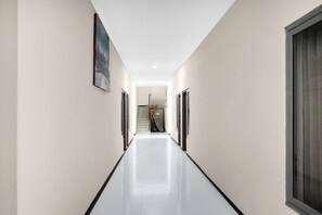 A long, narrow hallway with a polished floor, flanked by plain walls and doors on both sides.
