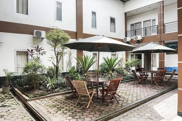 A courtyard with a table and chairs under umbrellas, surrounded by potted plants and a tiled floor.