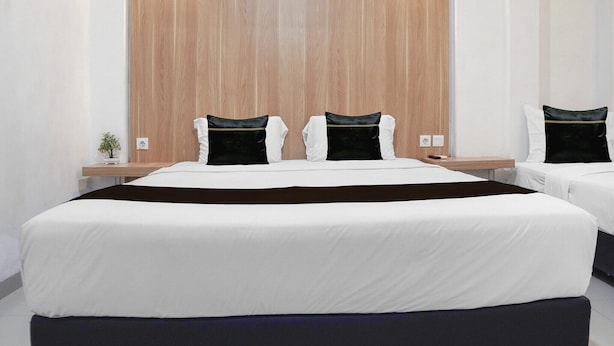 Habitación de hotel con dos camas, cabecero de madera, mesitas de noche y una planta pequeña.