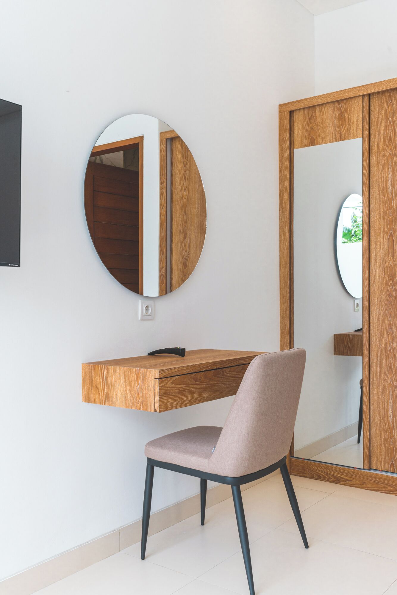 Ein modernes Zimmer mit Schreibtisch aus Holz, einem runden Spiegel und einem Stuhl.