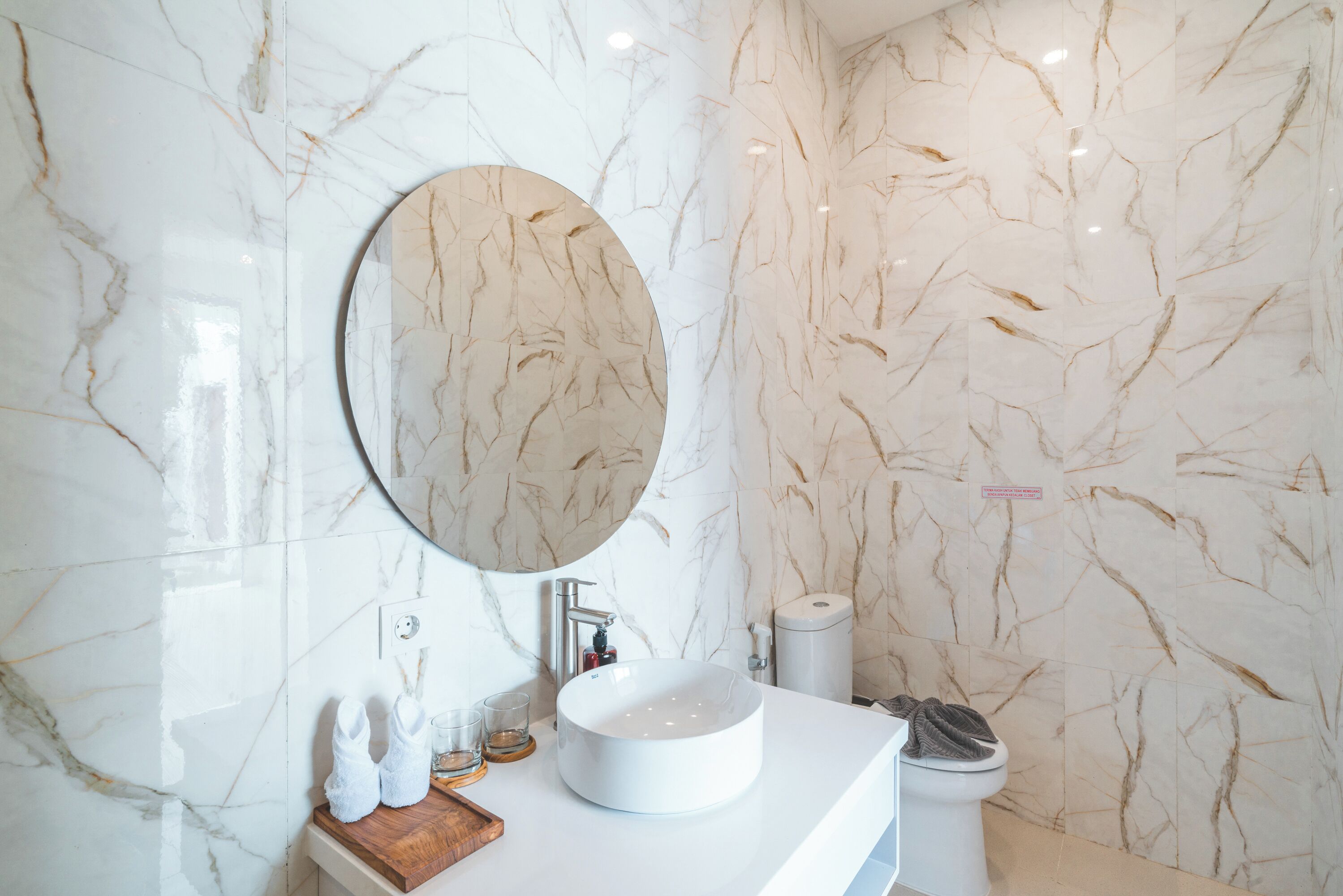 A bathroom with a marble sink, a round mirror, and a toilet.