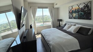 A modern hotel room with a large bed, a desk, a TV, and a cityscape painting. - Luxury Bridgeland 2BR/2BA – King Suite, Saddledome/City Views & Parking (Calgary)