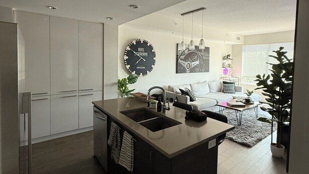 A modern kitchen with a central island, a dining area with a sofa and table, and a living room with a couch and a plant. - Luxury Bridgeland 2BR/2BA – King Suite, Saddledome/City Views & Parking (Calgary)