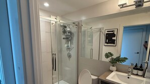 A modern bathroom with a glass-enclosed shower, a toilet, a sink with a mirror, and a potted plant. - Luxury Bridgeland 2BR/2BA – King Suite, Saddledome/City Views & Parking (Calgary)
