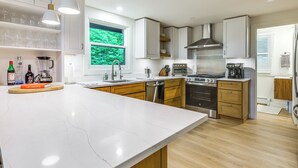 Een moderne keuken met witte kasten, een groot eiland, roestvrijstalen apparatuur en een raam met uitzicht op groen.