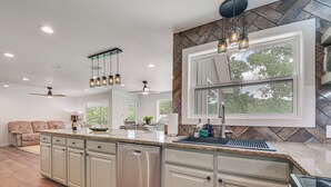 A modern kitchen with a dishwasher, stainless steel appliances, a large window, and a dining area with a sofa. - Bring Your Boats! Waterfront Retreat on PK Lake (Graford)