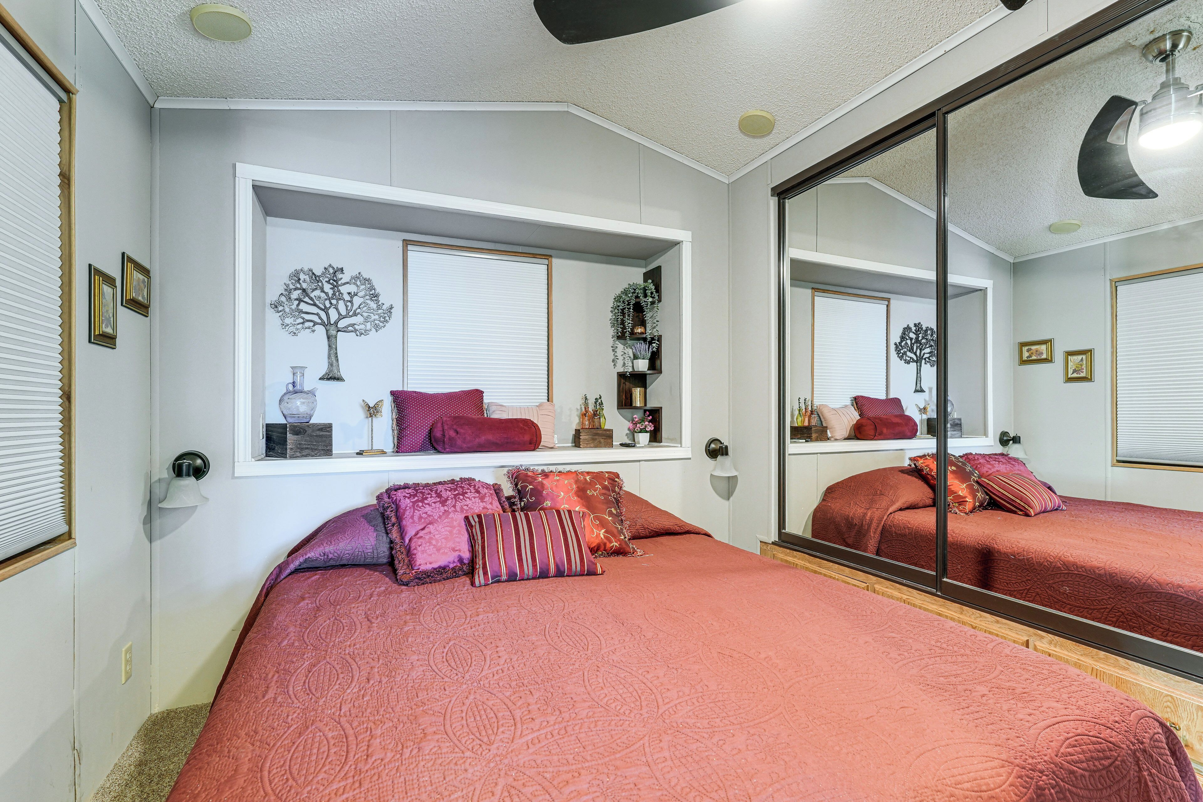 A bedroom with two beds, a large mirror, a window with a tree decoration, and a shelf with various items.