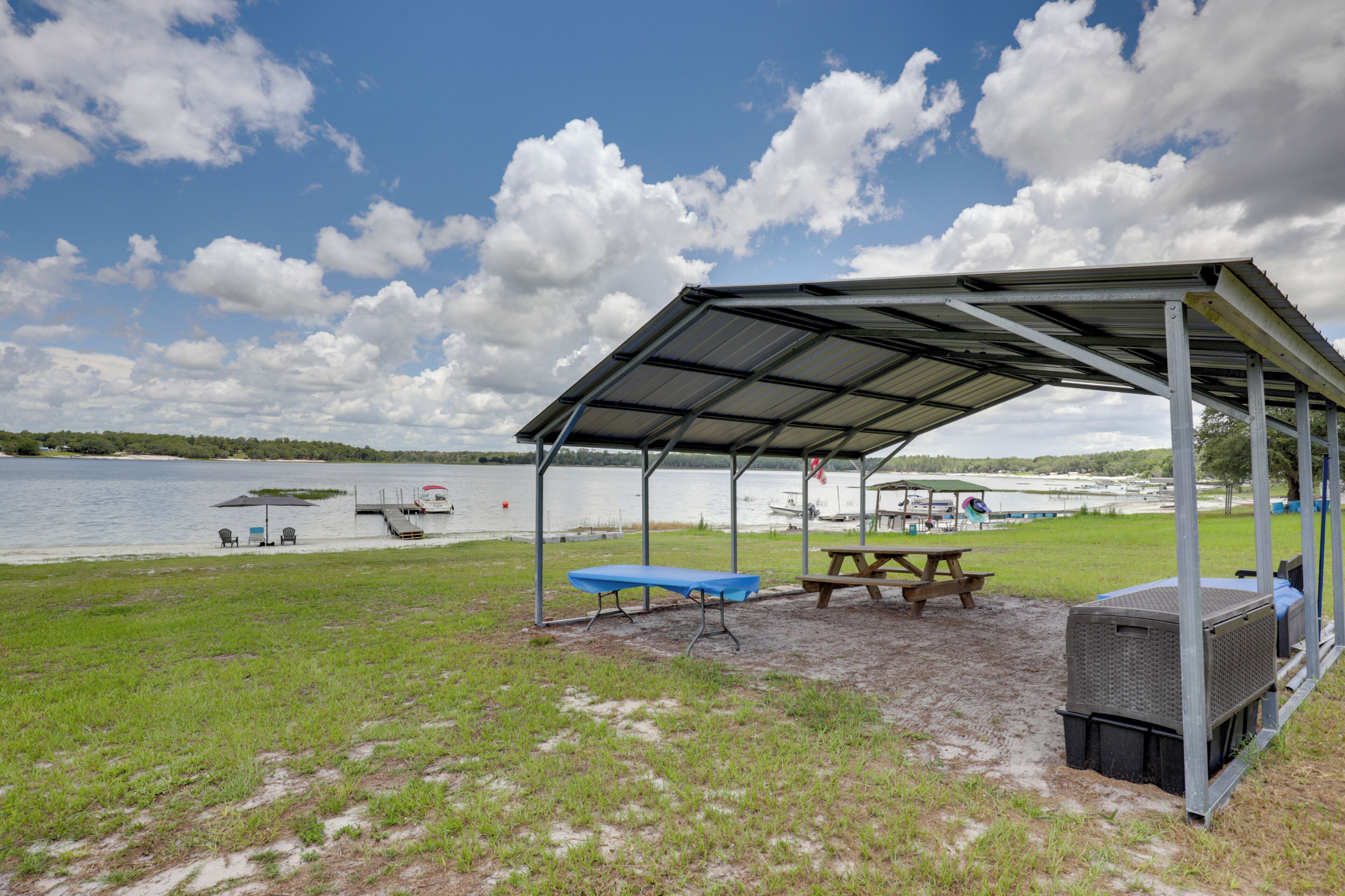 A covered picnic area with a table and benches, a portable grill, and a view of a lake with boats.