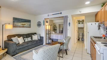 Un espacio habitable compacto con sofá, sillón, mesa de comedor, kitchenette y baño a la vista.
