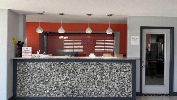 Un comptoir d’accueil avec un sol en terrazzo, un mur rouge et trois lampes suspendues.
