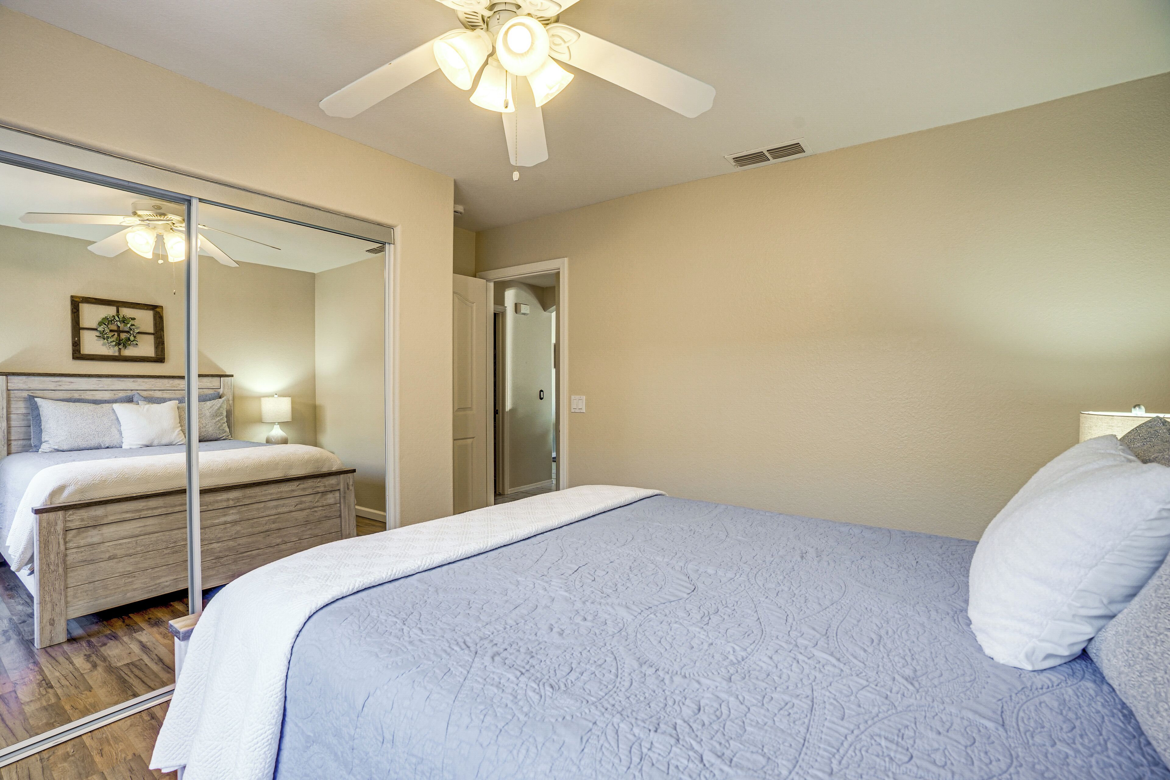 A bedroom with a bed, a ceiling fan, a mirror, and a door leading to another room.