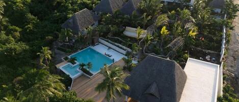 An aerial view of a resort with multiple buildings, a swimming pool, and lush greenery.