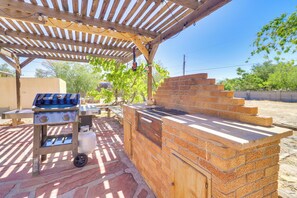 Un espace barbecue extérieur avec un gril et un four en briques, installé sous une pergola en bois.