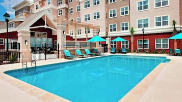 A hotel pool area with a clear blue pool, lounge chairs, and umbrellas.