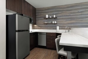 Una cocina moderna con gabinetes de madera oscura, un refrigerador de acero inoxidable, un microondas, un lavavajillas, una encimera de granito y un taburete de bar.