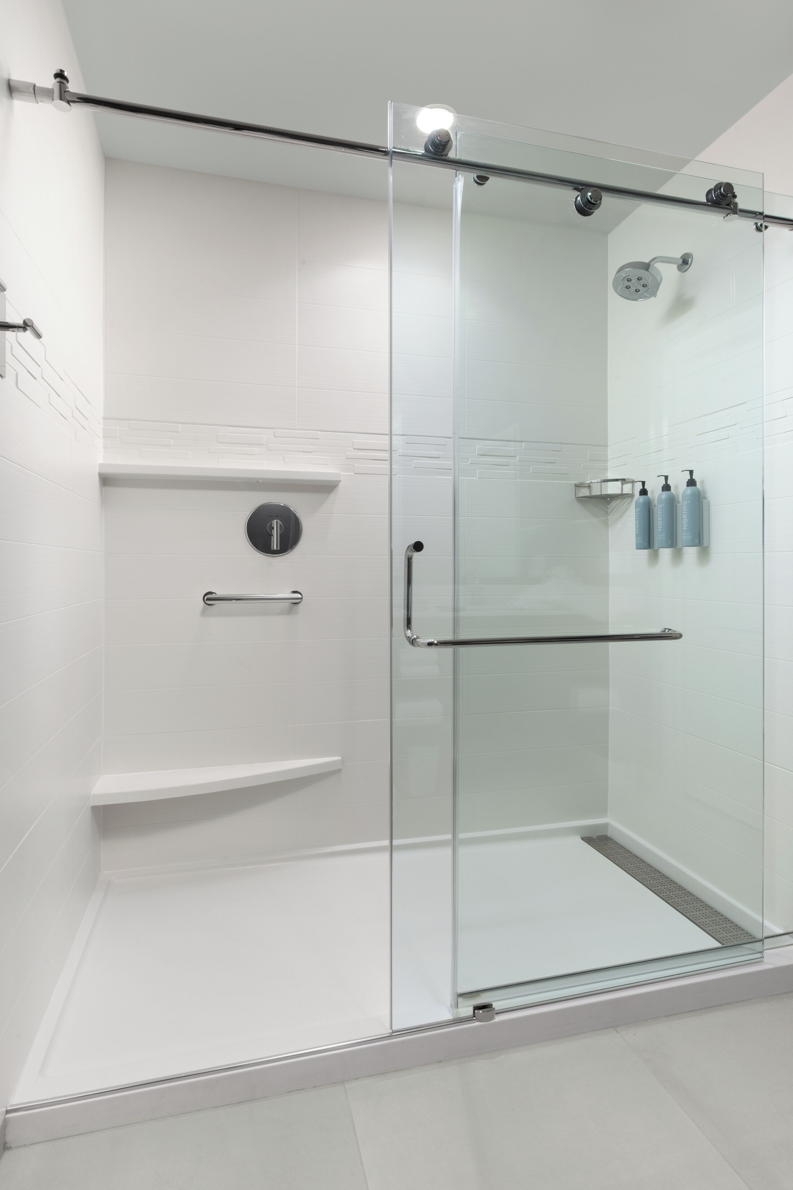A modern glass-enclosed shower stall with a glass door, a control panel, and a handrail.