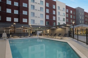 A swimming pool area with lounge chairs and umbrellas, surrounded by a multi-story building with large windows.