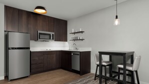 Eine moderne Küche mit dunklen Holzschränken, einem Edelstahlkühlschrank, einer Mikrowelle und einem Spülbecken. Es gibt eine Essecke mit einem Tisch und zwei Stühlen.