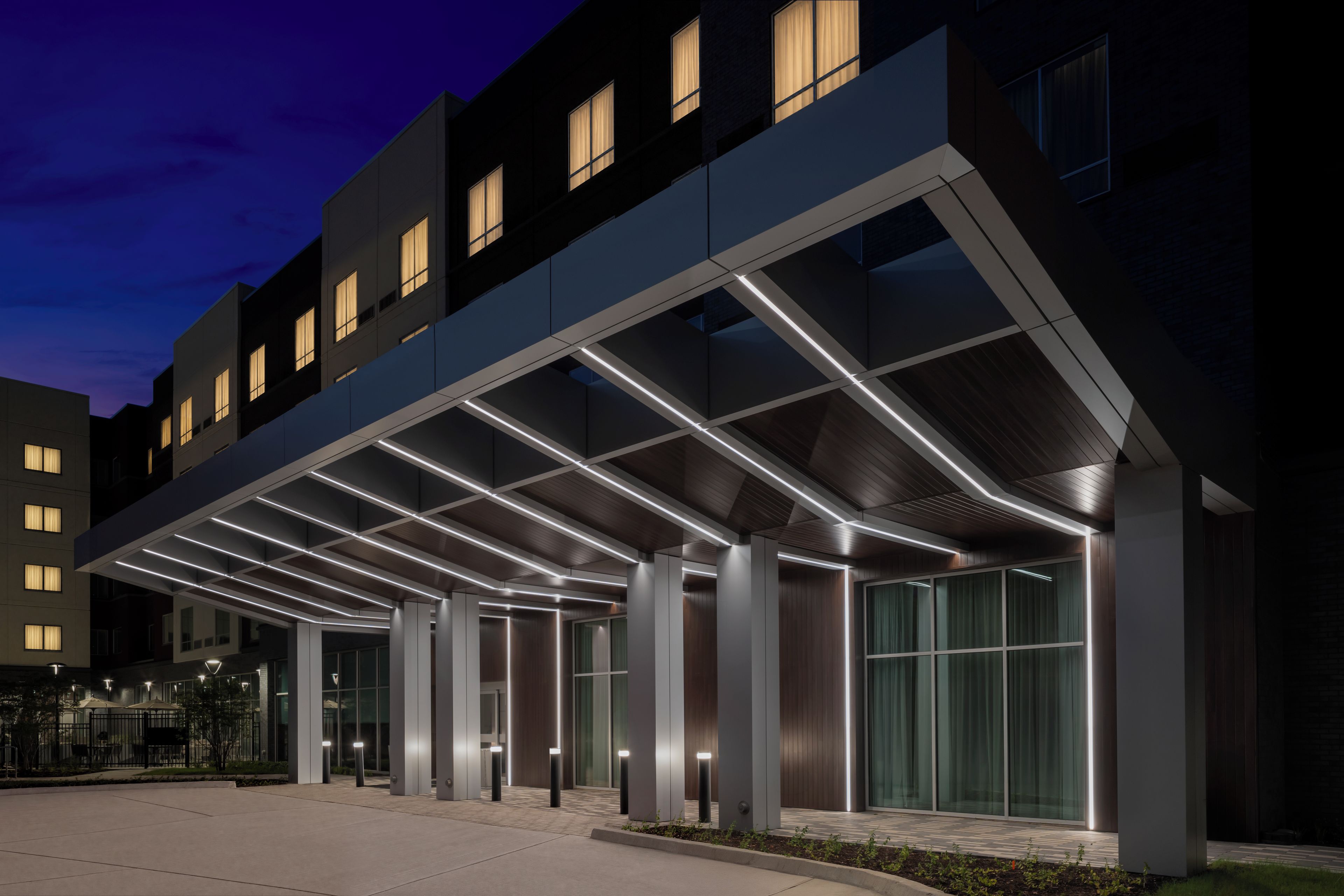 Una entrada de hotel moderna con un vestíbulo cubierto y columnas iluminadas.
