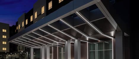 A modern hotel entrance with a covered walkway and illuminated columns.
