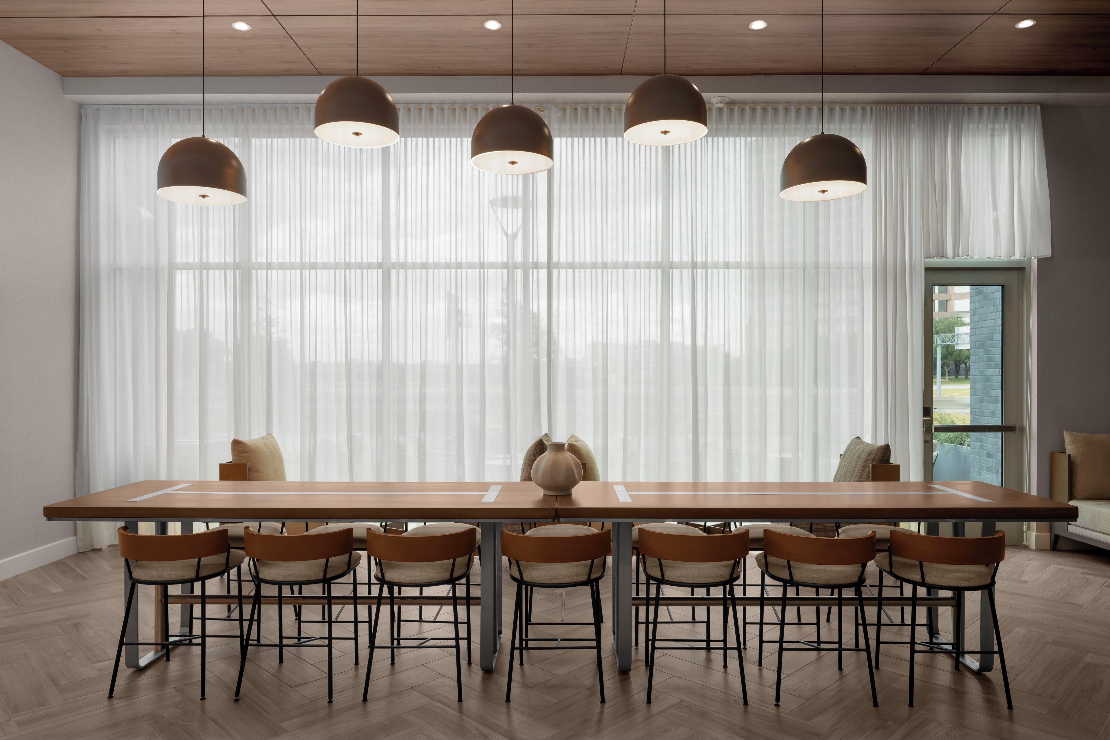 A modern dining area with a long wooden table, six chairs, and pendant lights.