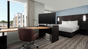 A hotel room with a bed, desk, chair, and a TV.