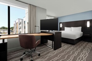 Habitación de hotel con cama, escritorio, silla y televisor.