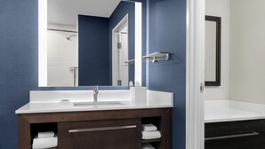 A modern bathroom with a white sink, a large mirror, and a dark wooden vanity with towels.